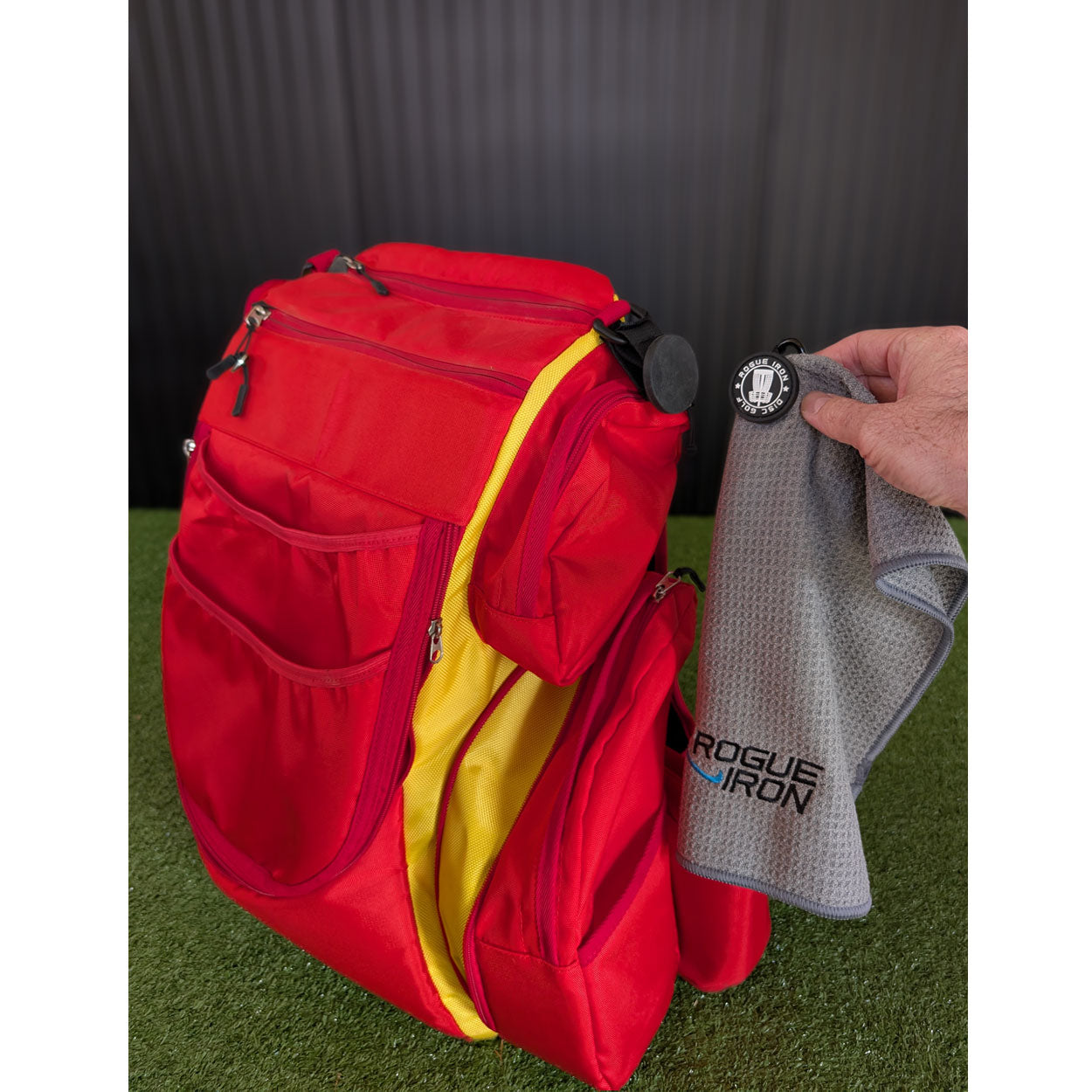 Disc golf towel strap attached to a backpack D-ring